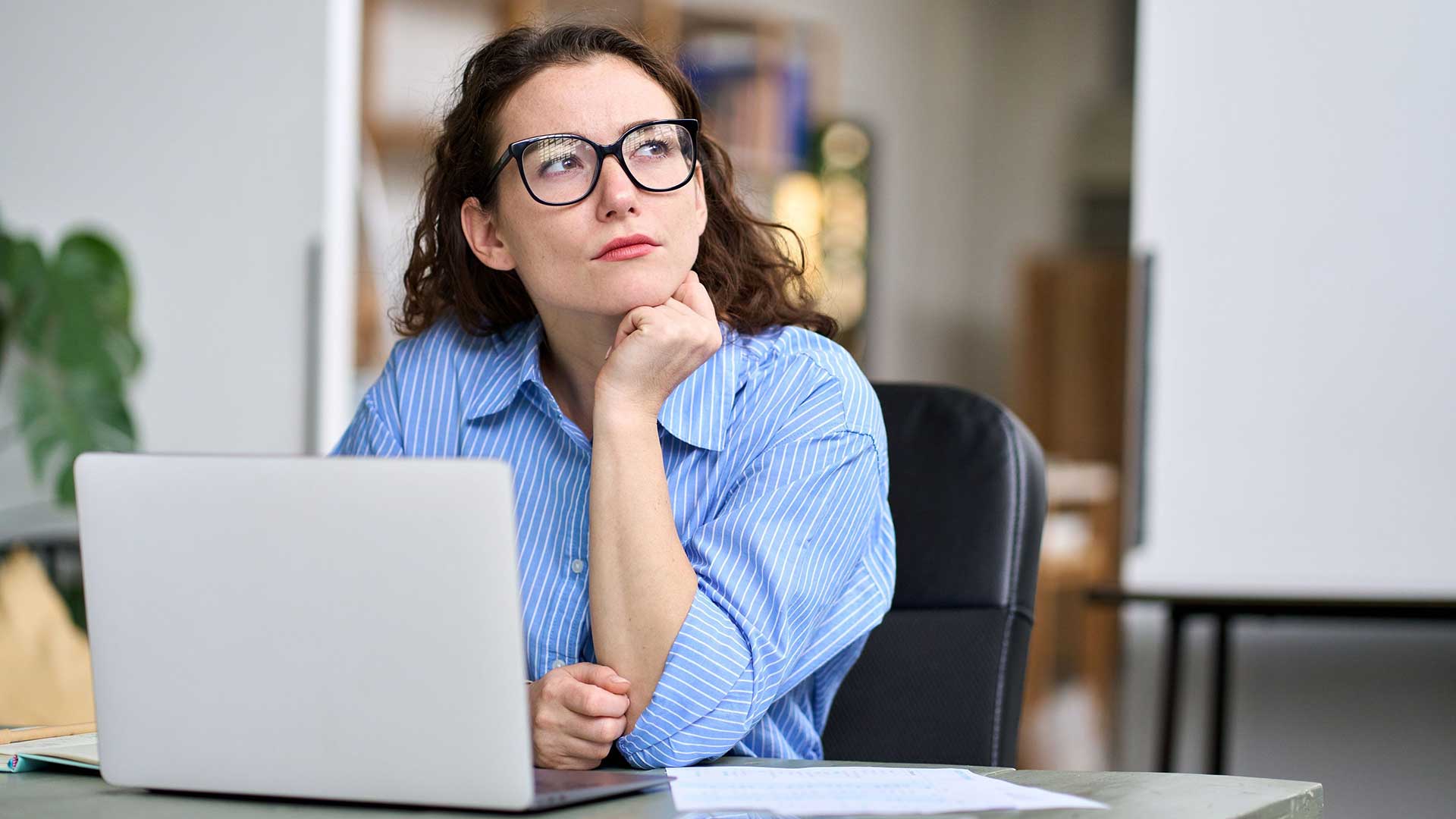 A woman sitting at a laptop and looking thoughtful