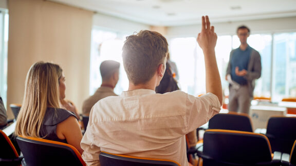 An audience member raising their hand to ask a question.