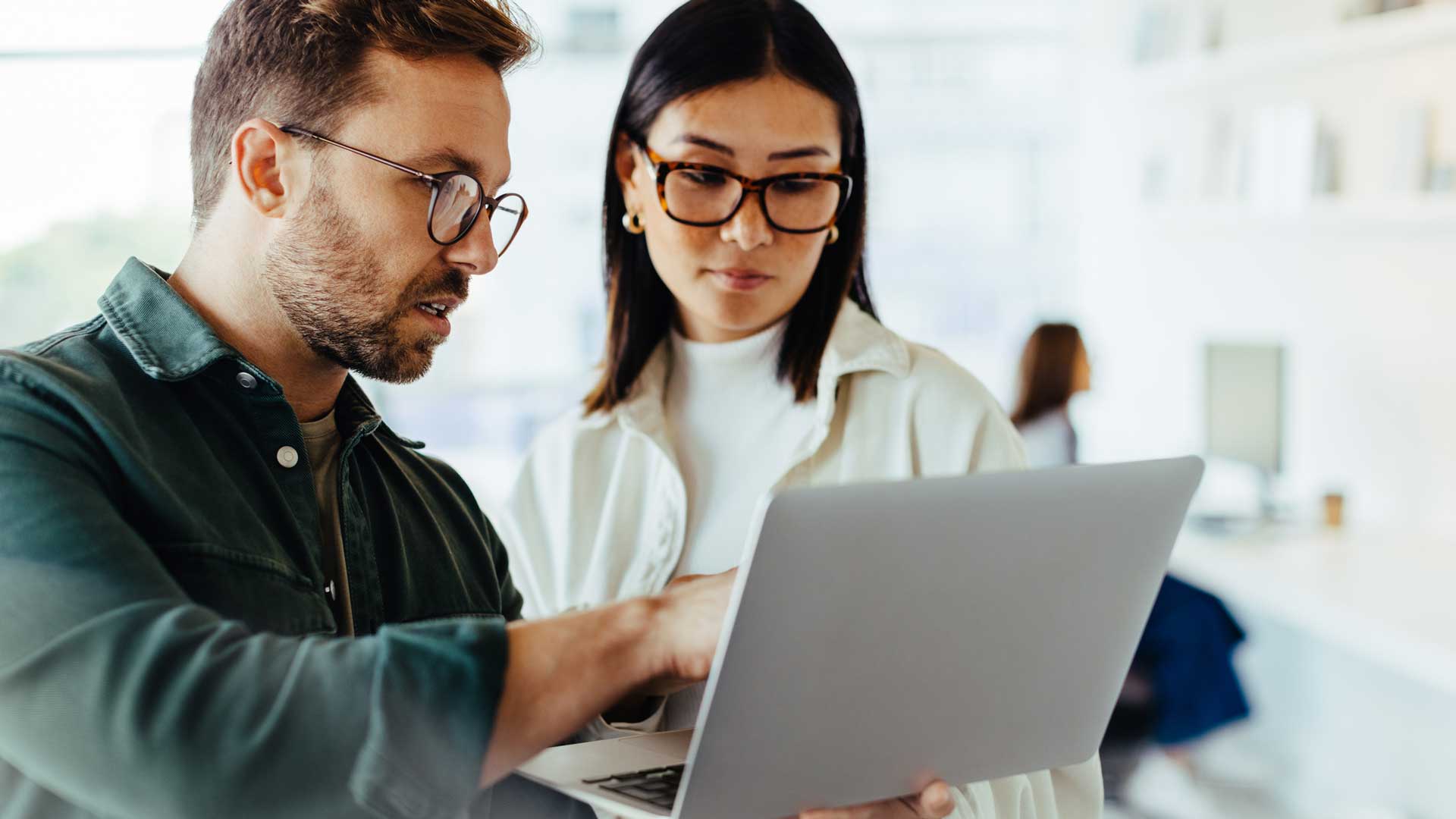 A man and a woman in an office look into a laptop and talk about a project