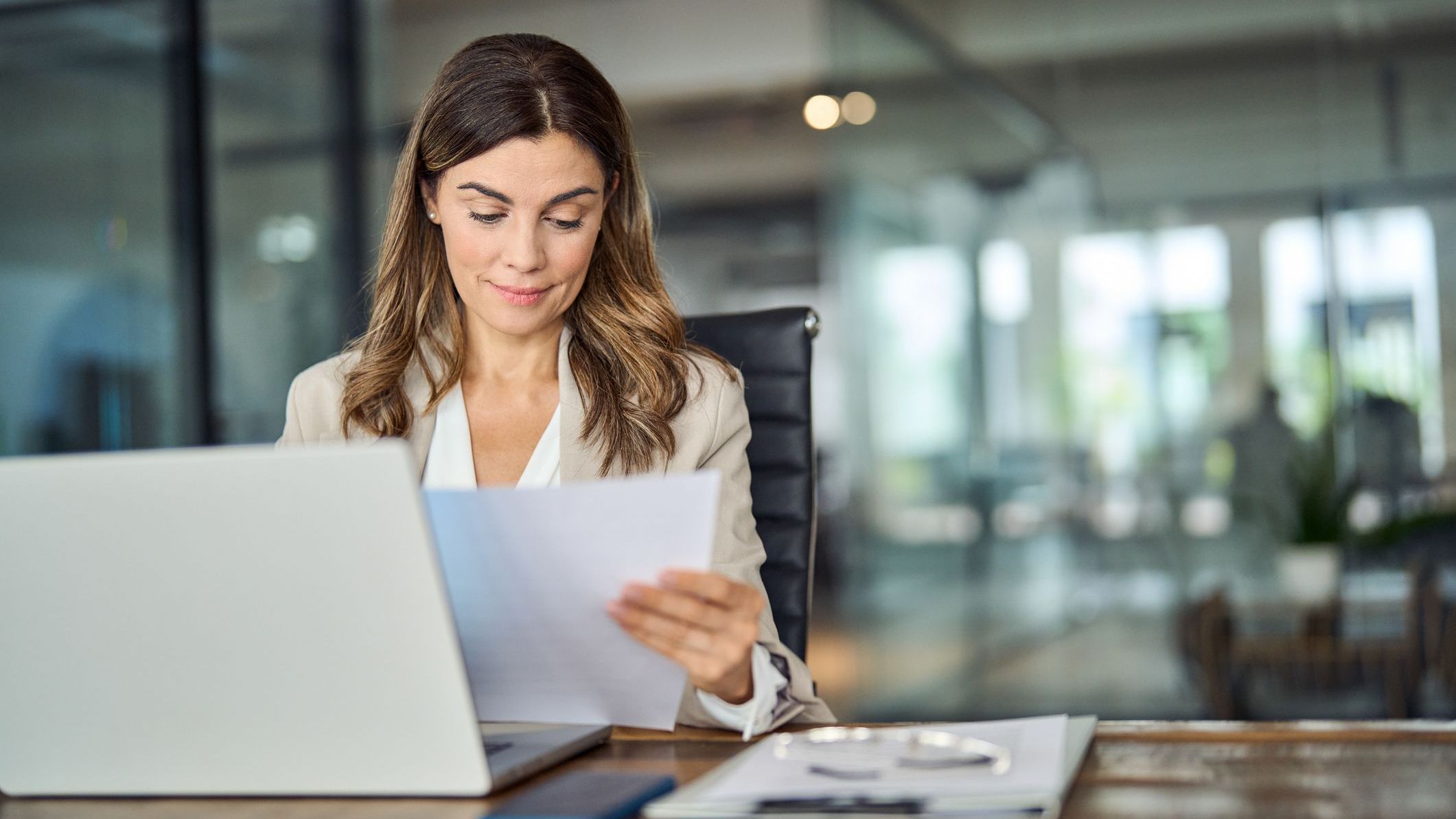 Business woman working in office with laptop reading document.